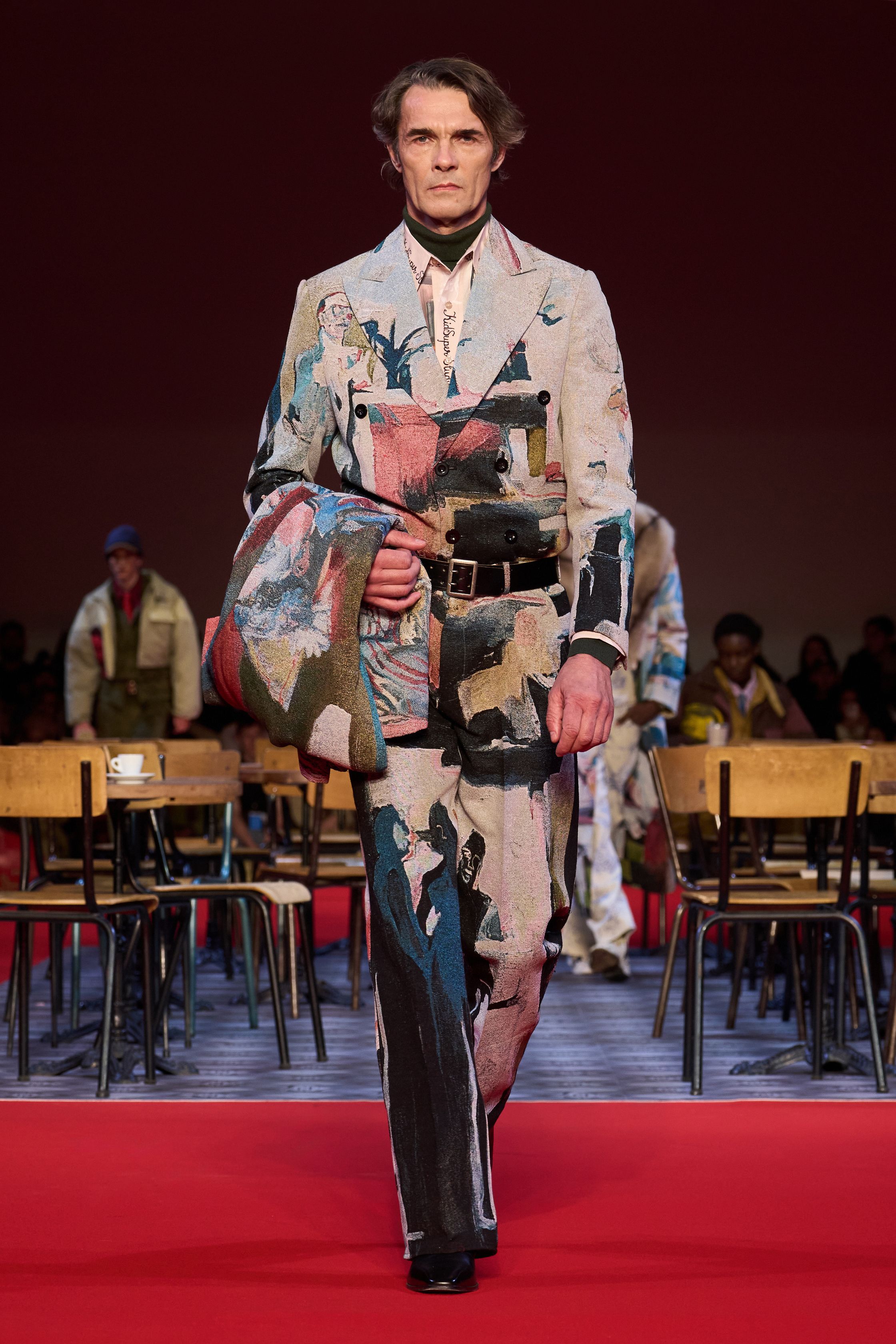 KidSuper 26FW 再次用“情绪拼贴”对抗工业化时尚秩序。手绘印花、夸张比例与情绪化色彩在红毯式秀场中被推向极致，服装不追求修饰身体，而是作为情感与记忆的载体存在。粗犷皮革、绘画感大衣与幼稚却真诚的图案语言并置，构成一种反精英、反理性的当代浪漫主义。KidSuper 依旧不完美，却极其真实-顽石频道趋势研究